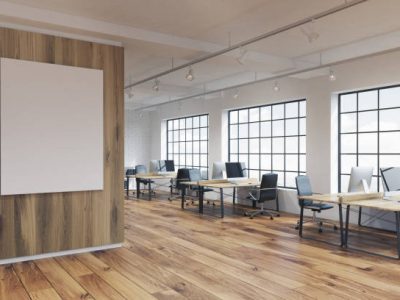 Corner of an office with a poster hanging on a wooden wall, rows of tables with computers and wooden floor. 3d rendering. Mock up
