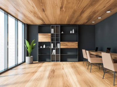Interior of modern coworking style office with grey walls, wooden floor and ceiling, long wooden table with beige chairs and laptops and bookcase. Window with blurry cityscape. 3d rendering